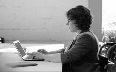 Une femme écrit sur son ordinateur portable assise à une table