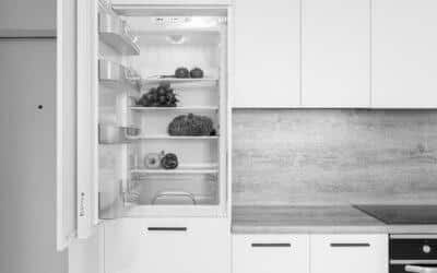 Un frigo avec la porte ouverte dans une cuisine blanche avec des légumes sur chaque étagères